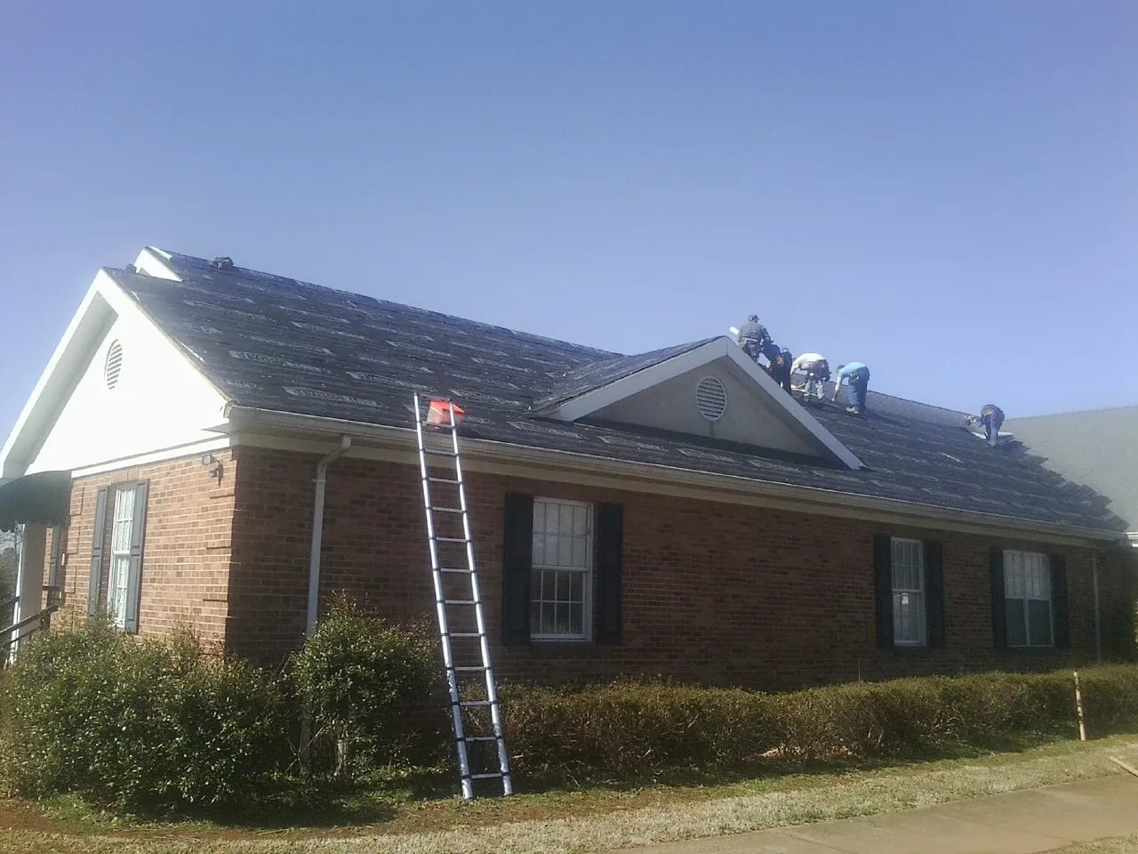 Crew tearing shingles off a brick ranch roof with a ladder set — Metal Roof Repair work by our crew in Valencia