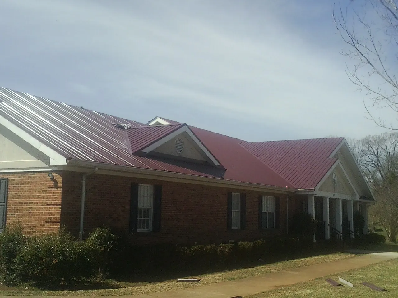 Red metal roof with gabled entries on a long brick building, from a Hail Damage Roof Repair job in Valencia